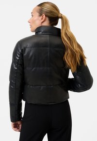 Sort læder pufferjakke med en cropped design, høj krave og blank tekstur. Har vandrette syninger og slanke ærmer.