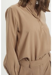 Langærmet blouse i lysebrun stof med en glat tekstur, der har en knaplukning og en afslappet pasform. Stylized med matchende bukser.