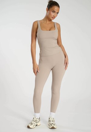 Beiges Sportbekleidungsset bestehend aus einem taillierten Tanktop mit quadratischem Ausschnitt und hochgeschnittenen Leggings. Glatter Stoff, minimale Details.
