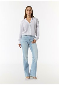 Lichtblauw overhemd met lange mouwen, gecombineerd met lichtgekleurde flared jeans en witte sandalen. Eenvoudig, strak ontwerp en lichte textuur.