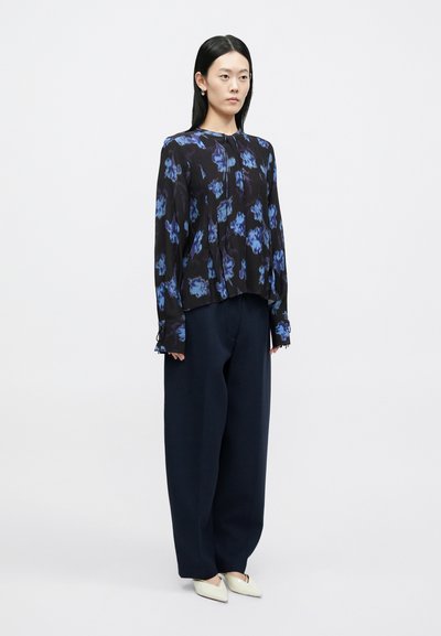 Μαύρο μπλουζάκι με μπλε λουλουδάτο μοτίβο, μακριά μανίκια, πιετές σχέδιο, σετ με σκούρο μπλε παντελόνι με φαρδύ πόδι και ανοιχτόχρωμα, μυτερά παπούτσια.