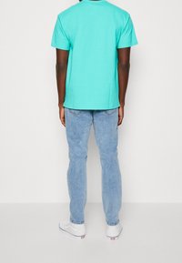 Turkos T-shirt med korta ärmar, klassisk passform, gjord av bomull, tillsammans med ljusblå jeans och vita sneakers.