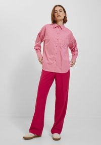 Red and white striped button-up shirt with a collar, paired with vibrant pink wide-leg trousers. The shirt features long sleeves and a relaxed fit.