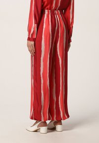 Pantaloni a gamba larga a righe rosse e crema con vita elastica, realizzati in tessuto leggero. Presentano una silhouette fluida e una consistenza morbida.