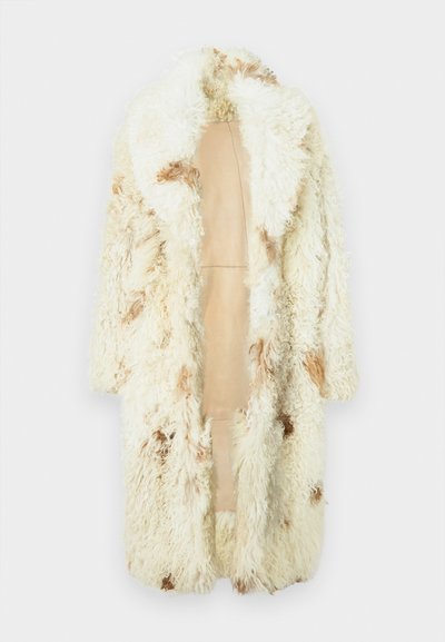 Garšs krēmkrāsas čihotā kažoks ar brūniem pleķiem, atvērta priekšpuse un mīksta tekstūra uz vienkāršota gaiša fona.