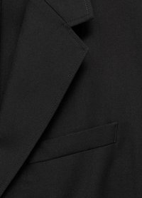 Blazer nero con rever a punta, tessuto textured e una tasca sul petto. Sono visibili dettagli di cucitura pulita.