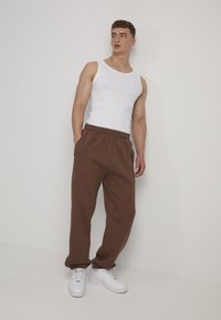 Jogging en tissu marron doux, avec une taille élastique et des poches sur les côtés, associé à un débardeur blanc ajusté et des baskets blanches.
