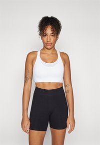 Hvit sporty crop top med skulderstropper, kombinert med høyt midje svarte shorts. Jevn tekstur, tettsittende design og minimalistisk stil.