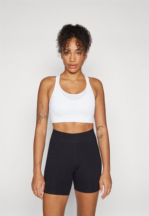 White athletic crop top with shoulder straps paired with high-waisted black shorts. Smooth texture, fitted design, and minimalistic style.