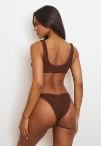 Completo bikini in maglia marrone con finitura testurizzata, caratterizzato da un scollo rotondo e spalline larghe per la parte superiore; il fondo ha un design a vita alta.