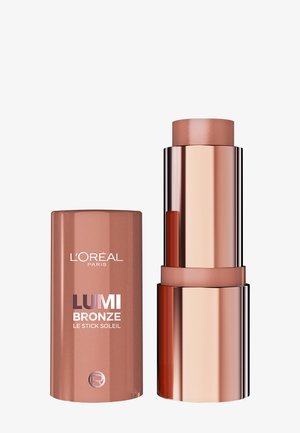 L'Oréal Lumi Bronze w sztyfcie ze zdjętym korkiem, ukazującym jasnobrązowy bronzer do makijażu w błyszczącym różowo-złotym opakowaniu.