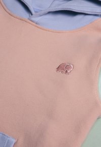 Haut sans manches rose clair avec une capuche bleue, arborant un petit logo en métal rose de ours sur le devant. Tissu doux avec une texture lisse.
