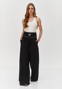 Czarne spodnie o szerokich nogawkach z wysokim stanem, z białymi przeszyciami i kieszeniami, zestawione z dopasowanym jasnym topem na ramiączkach.