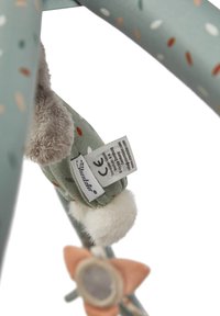 Soft toy attachment with a green fabric adorned with colorful dots, a fluffy tail, and a label featuring safety information. Flower-shaped accent included.