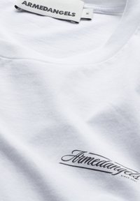 Weißes Baumwoll-T-Shirt mit V-Ausschnitt, versehen mit einem kleinen schwarzen Aufdruck, der "Armedangels" auf der unteren Vorderseite zeigt. Leichter Stoff.