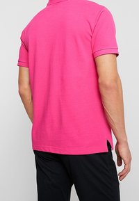 Polo a maniche corte in cotone rosa brillante con colletto a costine, spacchi laterali e dettagli di cucitura a contrasto lungo le maniche.