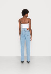 Jeans de denim azul claro com corte reto e cintura alta, apresentando dois bolsos traseiros e uma etiqueta laranja na cintura.