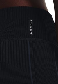Leggings sportivi neri con una texture a coste, caratterizzati da una striscia blu a contrasto e un'etichetta con logo ricamato che recita "RUSH" sulla vita.