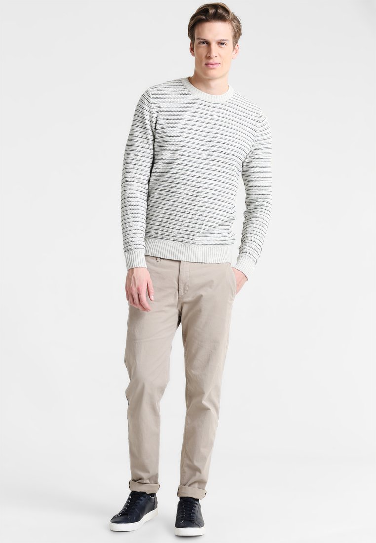 Hellgrau gestreifter Pullover mit Rundhalsausschnitt, beigen Chinos und schwarzen Schnürsneakern. Das Outfit zeichnet sich durch ein lässiges Design mit gerippten Bündchen aus.