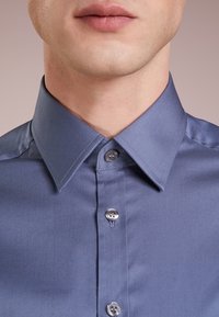 Lichtblauw overhemd met puntkraag, knoopsluiting met zilverkleurige knopen, gemaakt van gladgeweven stof.