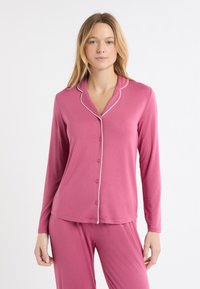 Różowa piżama z długim rękawem, zapinana na guziki, z białym obszyciem przy kołnierzu, wykonana z miękkiego materiału, w komplecie z dopasowanymi różowymi spodniami.