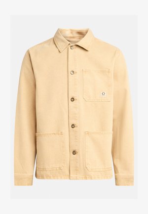 Beżowa bawełniana kurtka z kołnierzem, z zapinaniem na guziki z przodu, dwoma dużymi kieszeniami oraz małą metką z logo na kieszeni piersiowej. Gładka tekstura.