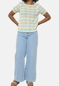 Top de mangas cortas con un patrón de zigzag multicolor, combinado con pantalones vaqueros de pierna ancha de color azul claro y sandalias de tacón abierto color canela.