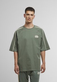 Groen oversized t-shirt met korte mouwen, crèmekleurige zijstroken en een logo patch op de linkerborst. Gemaakt van lichtgewicht katoen.