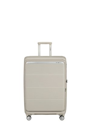 Beige hard-shell suitcase with horizontal ridges, adjustable handle extended, four spinner wheels, and Samsonite logo near top edge.
