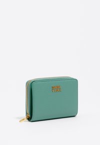 Portafoglio verde menta realizzato in pelle testurizzata, con zip dorata e logo. Forma rettangolare con bordi arrotondati, design compatto.