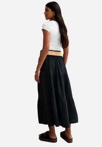 Gonna maxi nera, con texture e design a balze, abbinata a una t-shirt bianca attillata e scarpe slip-on nere con un accento intrecciato.