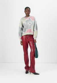 Maglione grigio con motivo floreale e maniche a palloncino abbinato a pantaloni in pelle rossi a vita alta, che tiene una borsa verde e indossa décolleté neri a punta.