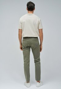 Camiseta corta de manga beige claro metida dentro de pantalones ajustados verde oliva, combinada con zapatillas blancas; bolsillos traseros visibles y detalles de costura.
