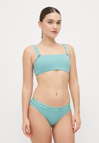 Et to-delt badetøysett i lys turkis med bandeau-top og lavt bikinibunn, med logo-acenterte stropper og midje.