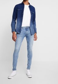 Jeansskjorta i mörk till ljus gradient blå, knäppning framtill med bröstfickor, tillsammans med ljusblå slim fit jeans och vita sneakers.
