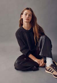 Mørk, struktureret striktrøje med rund hals, kombineret med skinnende sorte bukser i imiteret læder og sporty beige-brune sneakers.