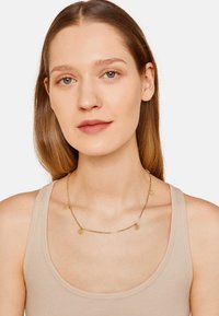 Gouden collier met een delicate ketting en kleine ronde pendants, dat mooi aansluit bij een neutraal gekleurd tanktop. Eenvoudig, vrouwelijk ontwerp.