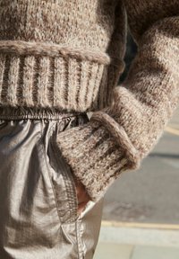 Tjockstickad tröja i beige nyanser med ribbad nederkant och ärmslut, tillsammans med byxor i lätt metallisk tyg med elastisk midja.