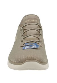 Beige athletic shoe with a mesh upper, lace-up design, and a white rubber sole. Features a tag indicating machine washable capability.