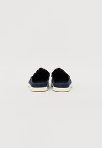 Mørkeblå slip-on-sko med teksturert overdel, bølgete kant og hvit gummisåle, med en minimalistisk design uten synlige mønstre.
