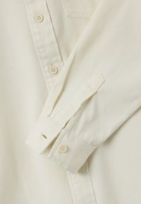 Roomkleurig katoenen shirt met een getextureerd oppervlak, voorzien van een knoopsluiting en knoopmanchetten. Inclusief een klein schouderpatch.