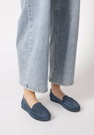 Niebieskie zamszowe buty wsuwane z teksturowanymi detalami na górze i gumową podeszwą, połączone z jasnoniebieskimi spodniami dżinsowymi w szerokim kroju.