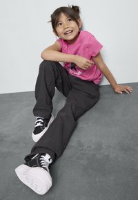 T-shirt rosa con grafica circolare nera, abbinato a pantaloni neri larghi e sneakers nere con suole e lacci bianchi.