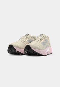 Lys beige løpesko med rosa mellomsole, svarte yttersåler og grå sidemønstre, vist fra en lav frontvinkel på hvit bakgrunn.