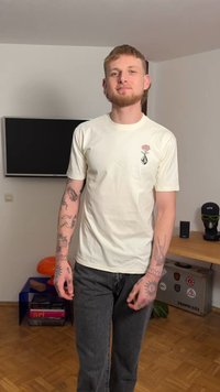 Kurzärmeliges cremefarbenes T-Shirt mit einem aufgedruckten Rosen- und Diamantdesign auf der linken Brust, kombiniert mit dunkelgrauen Jeans.
