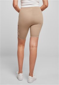 Beige fietsbroek gemaakt van rekbaar materiaal, met een kanten paneel aan de linkerkant. De broek is aansluitend en heeft een lengte tot halverwege de dij.