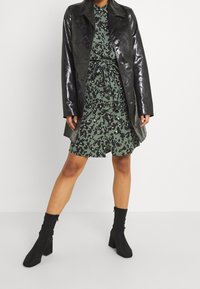 Svart, glansig läderjacka över en grön klänning med svart leopardmönster, knäppt med ett bälte i midjan, tillsammans med svarta ankelskor.