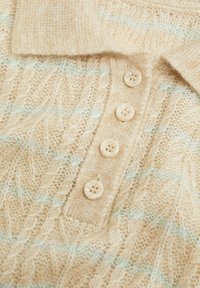 Polo shirt lavorato a maglia beige con un motivo testurizzato, dotato di colletto e quattro bottoni chiari lungo la patta. Presenti accenti blu sottili.