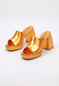 Mules de plataforma metálicos en color naranja con punta abierta, parte superior ancha y tacón grueso. Textura suave con un acabado brillante.
