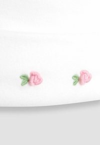Tissu blanc avec des roses brodées en rose clair et des feuilles vertes, disposées en ligne droite le long de l'ourlet. Texture lisse.